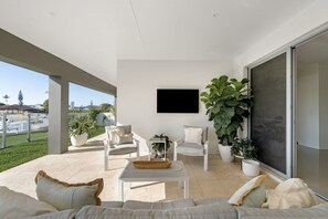 A modern living room with a flat-screen TV, comfortable seating, and large potted plants. - Luxe Family Entertainer on Canal Private Pool (Gold Coast)