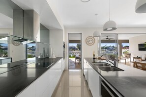 A modern kitchen with a glass cooktop, stainless steel appliances, and a view through a glass door to an outdoor patio. - Luxe Family Entertainer on Canal Private Pool (Gold Coast)
