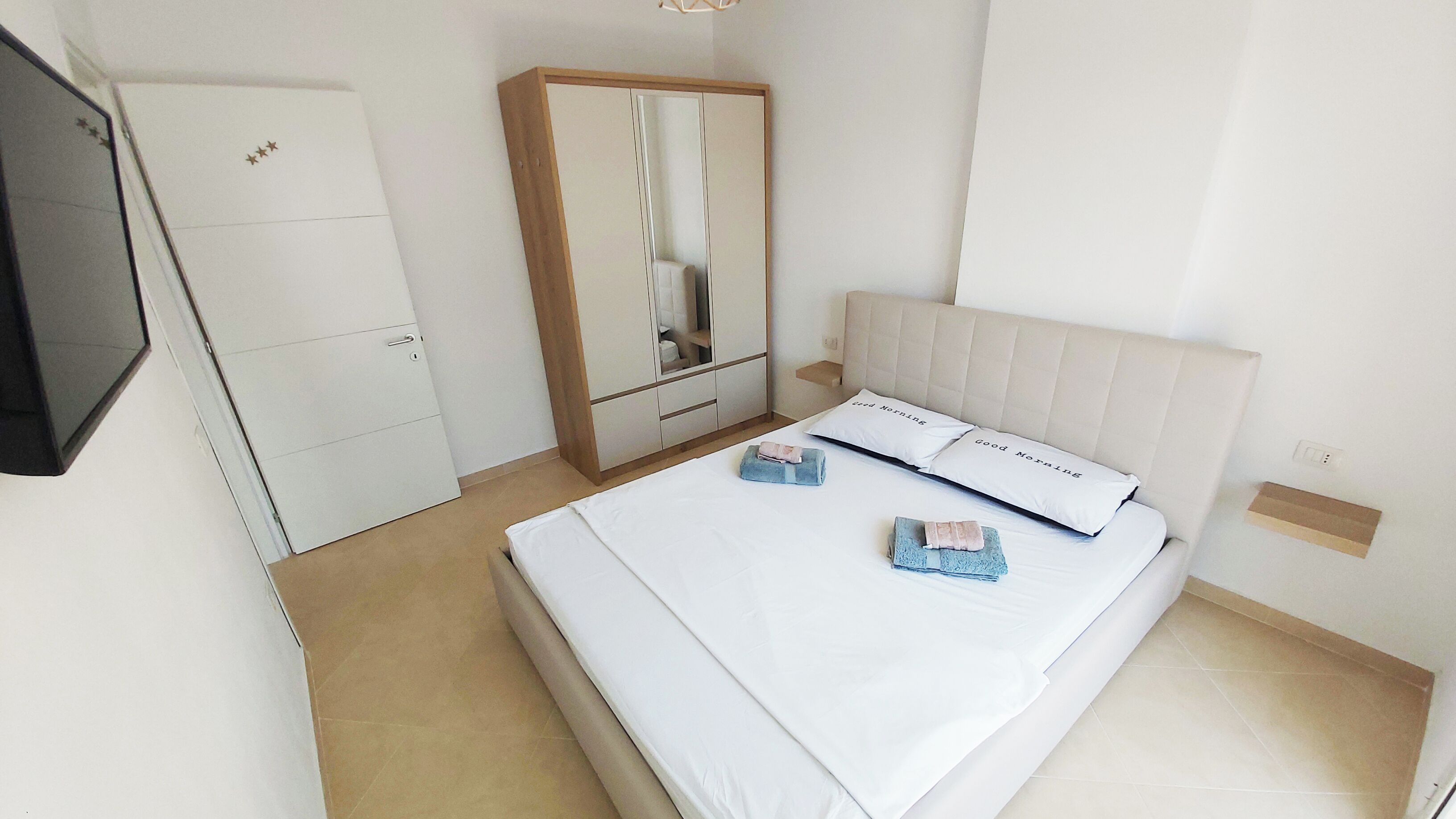 Ein ordentlich eingerichtetes Hotelzimmer mit Bett, Schrank, Spiegel und Fernseher.
