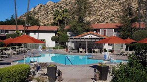 A pool area with lounge chairs and umbrellas, a pool, and buildings with red roofs in the background. - Ramona | Family Country Retreat | Pool + Tennis | 2BR (Ramona)