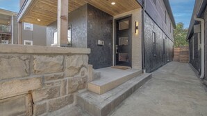 Un edificio moderno con fachada de piedra, terraza de madera y puerta metálica.