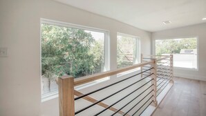 Una habitación amplia con ventanas grandes, barandilla de madera y vistas al exterior a zonas verdes.