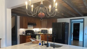 A kitchen with wooden cabinets, a black refrigerator, a marble island with a sink, and a chandelier.