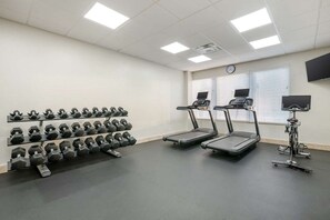Ein Fitnessstudio mit Laufbändern, Hanteln und einer Uhr an der Wand.