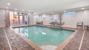 An indoor swimming pool with a tiled floor, a glass barrier, and a view of palm trees outside.