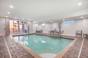 Una piscina interior con suelo de baldosas, barrera de vidrio y vistas a palmeras.