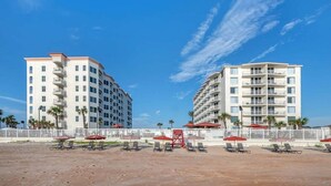 A beachfront hotel with multiple floors, outdoor seating, and a white fence.