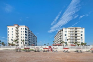 Un hotel frente a la playa con varios pisos, terraza exterior y cerca blanca.