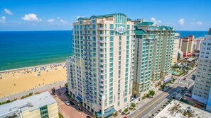 A high-rise hotel with multiple balconies, a beach view, and a clear sky.