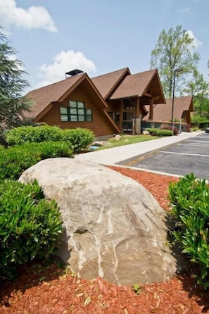 A building with a sloped roof, large windows, and a stone feature in the foreground.