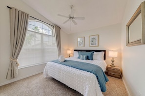 Quarto com cama, duas luminárias de cabeceira, ventoinha no teto e janela com cortinas.