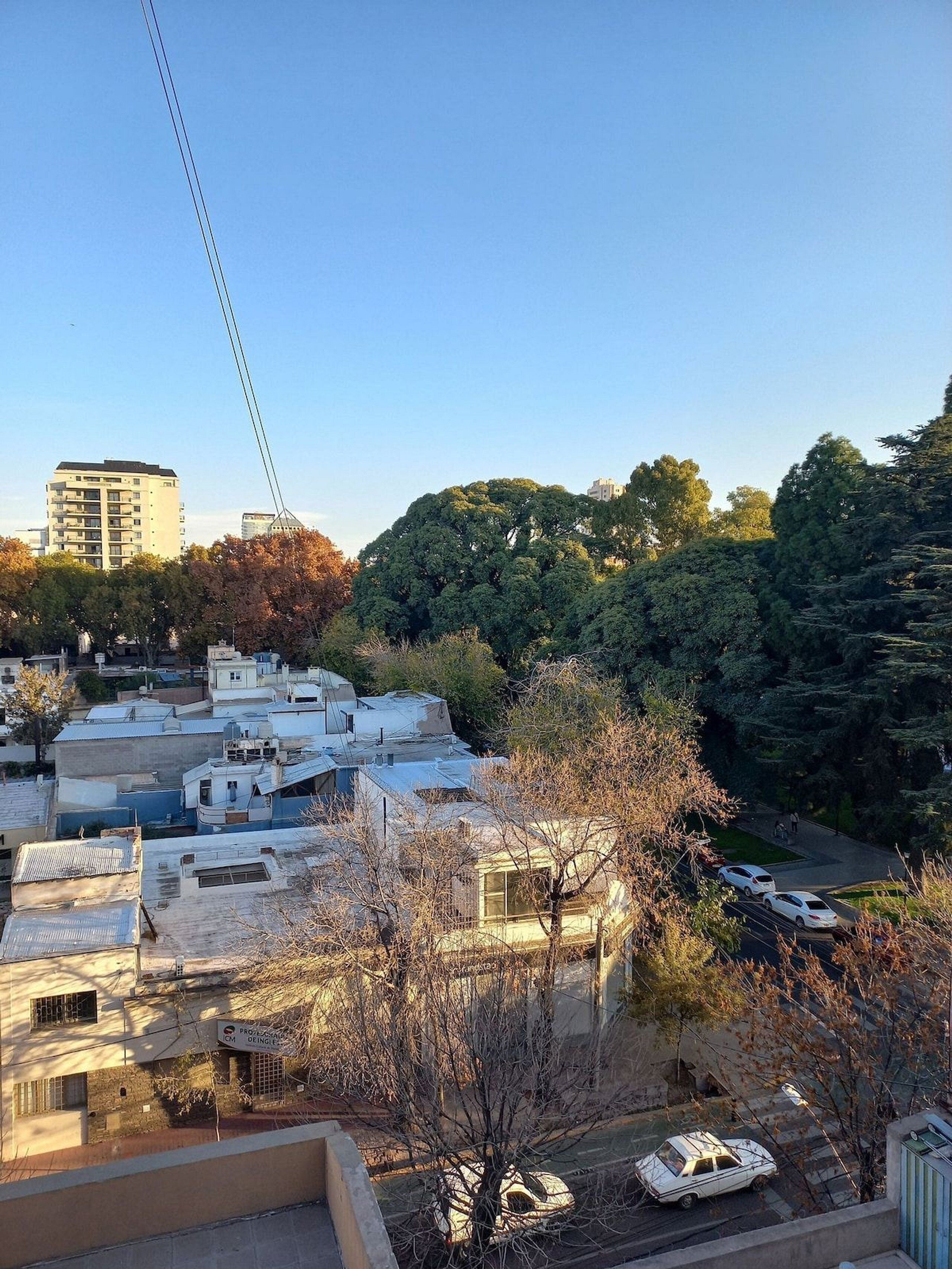 Zona residencial con varios edificios, algunos con techos planos y otros con tejados inclinados. Se ven árboles al fondo y un cielo despejado.