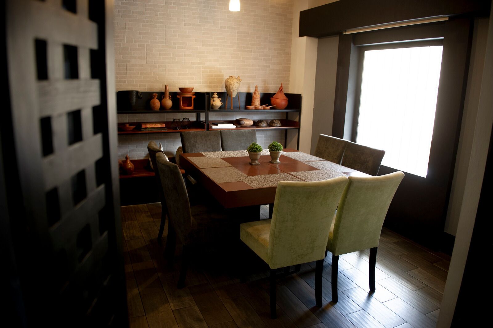 Un comedor con una mesa de madera, sillas acolchadas y estantes con objetos decorativos.