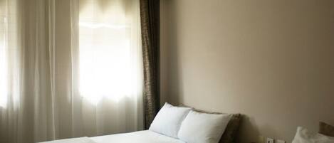 Ein Hotelzimmer mit zwei Betten, einem Deckenventilator und einem fensterbepflanzten Fenster.
