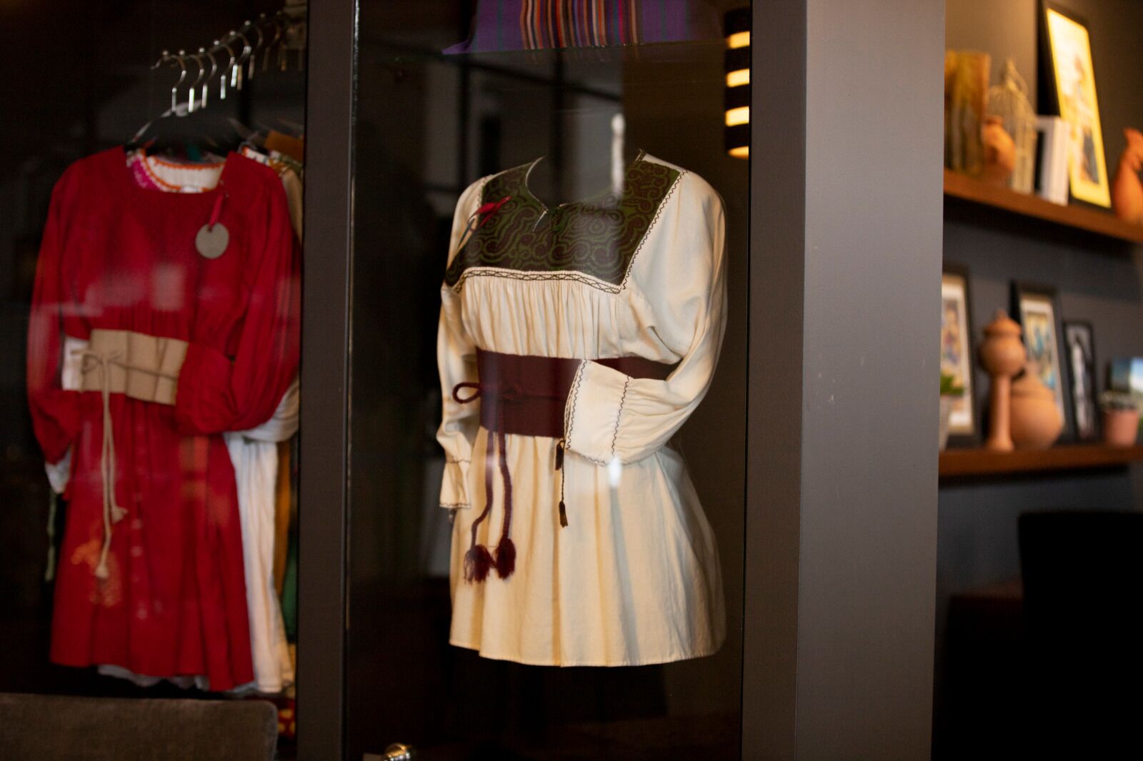 A display of traditional clothing on hangers, including a red dress and a white blouse with a brown belt.