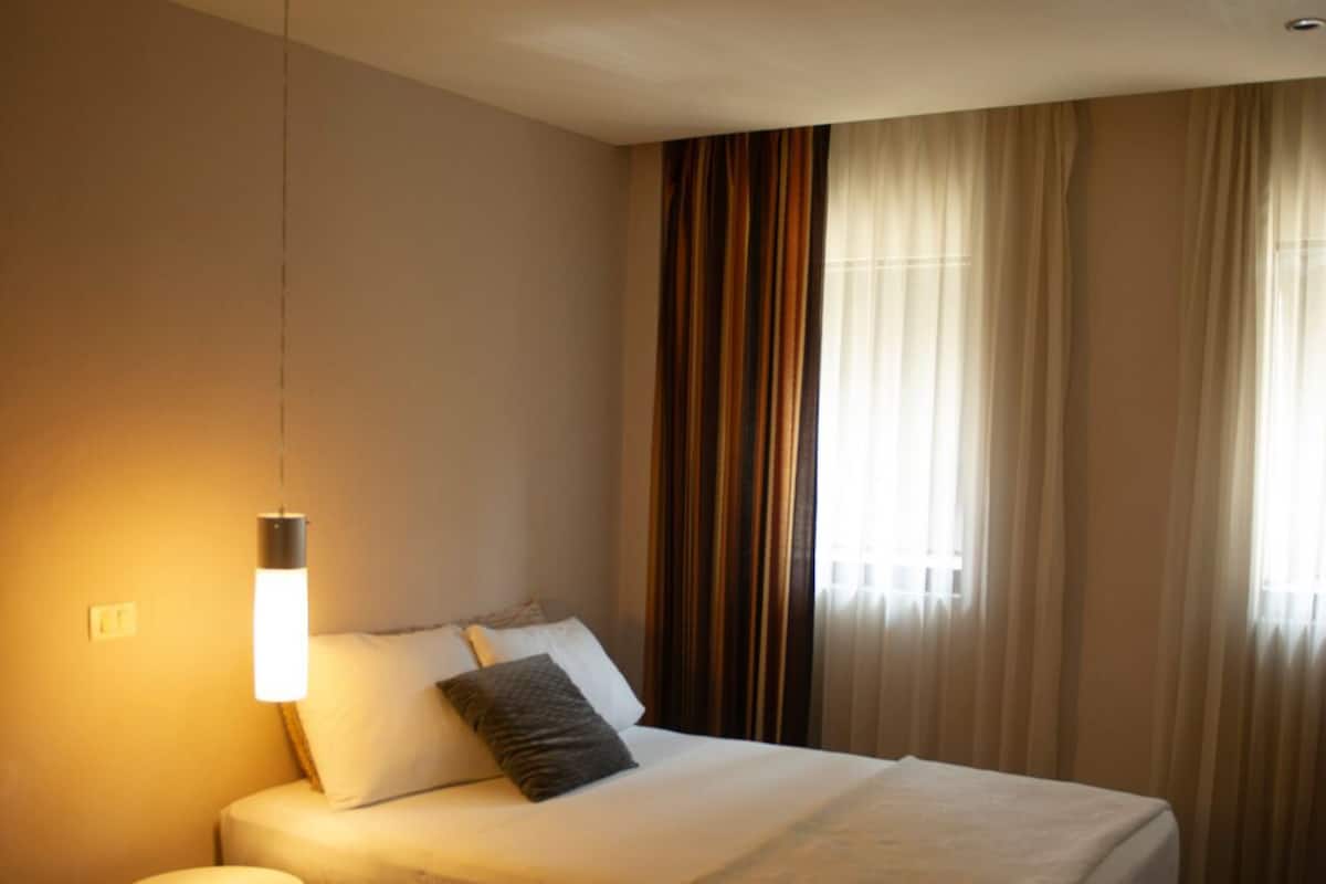 A neatly made bed with a white comforter and pillows, a bedside lamp, and a small rug on the floor.
