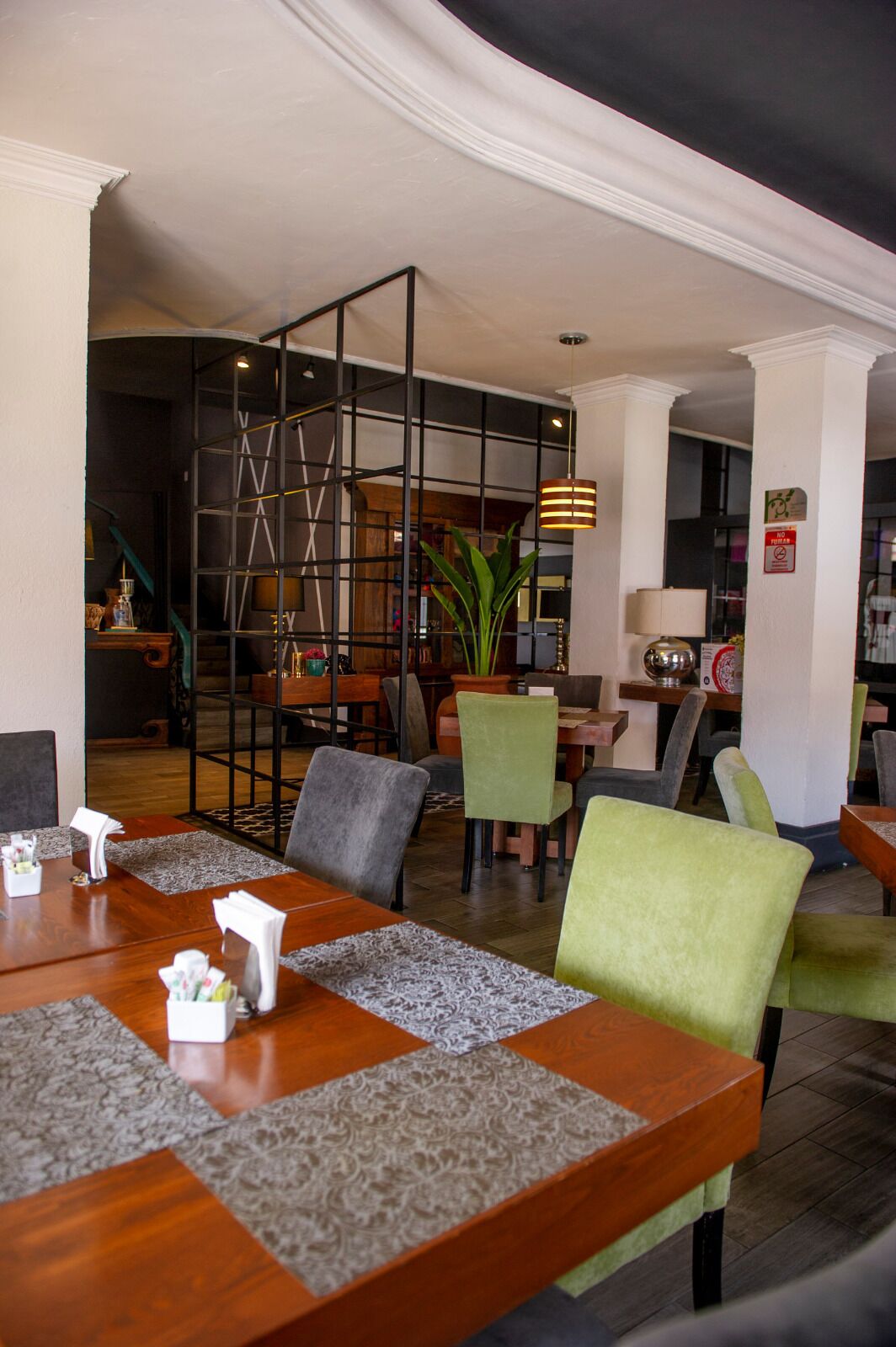 A dining area with wooden tables, green and grey upholstered chairs, and a black metal partition.