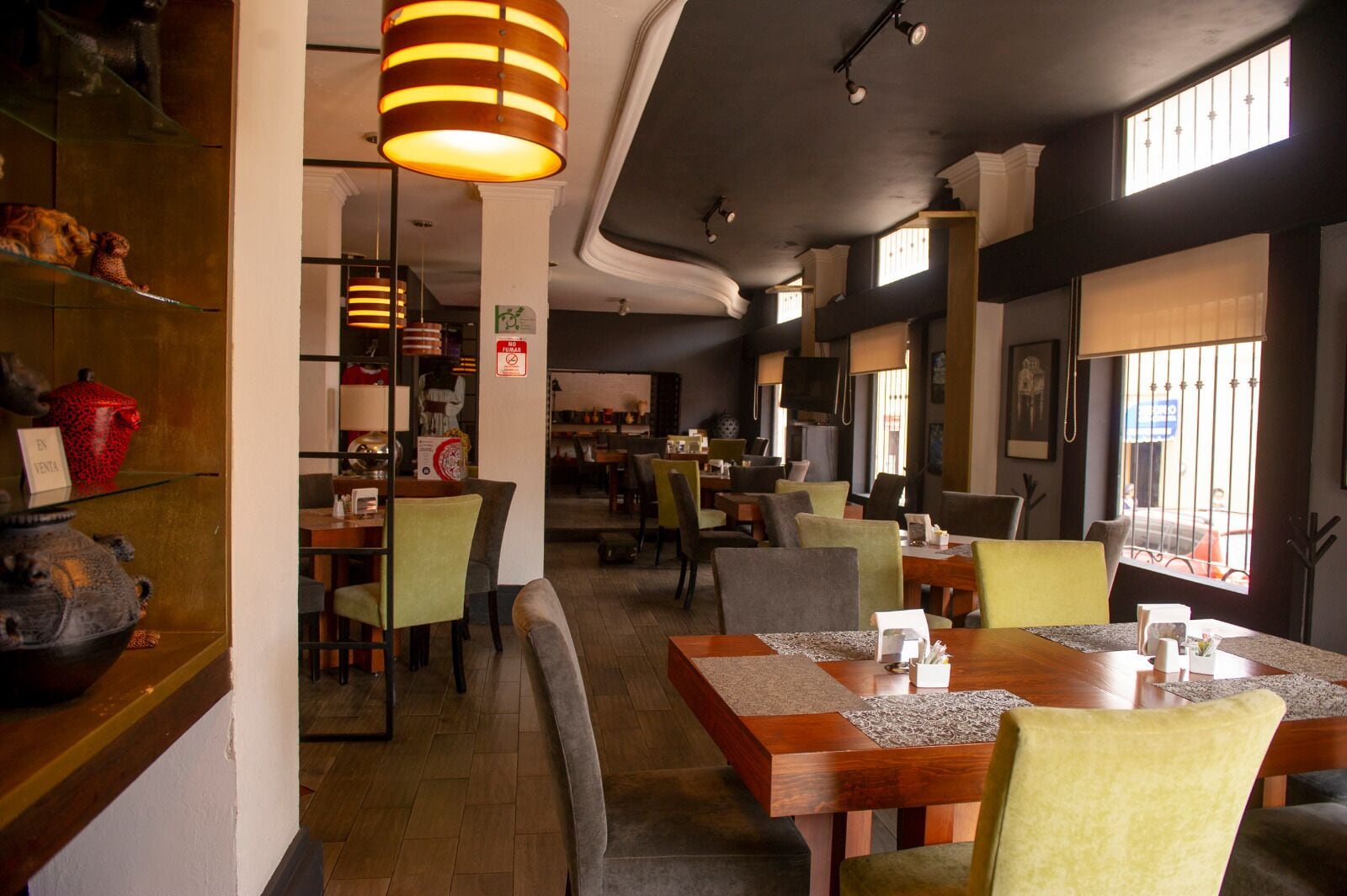 A restaurant with wooden tables and chairs, hanging lamps, and a view of the street through large windows.
