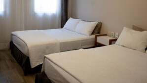 Habitación de hotel con dos camas, ventilador de techo y ventana con cortinas.