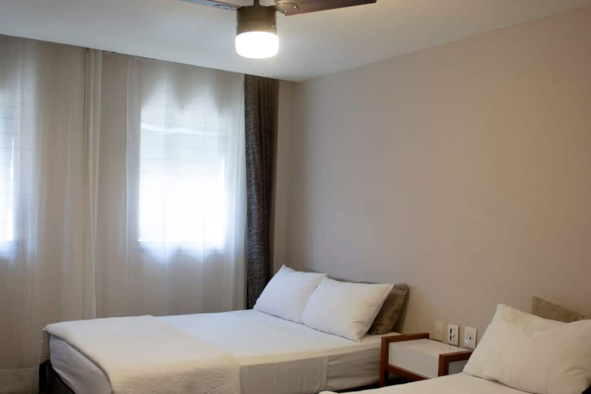 A hotel room with two beds, a ceiling fan, and a window with curtains.