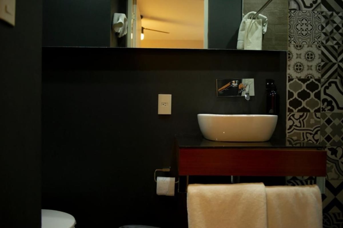 Un baño moderno con un lavamanos blanco, pared oscura y baldosas estampadas.