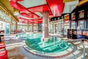 Une piscine avec un bord carrelé, un pilier central et une enceinte en verre.