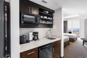 Een kleine hotelkeuken met een magnetron, koffiezetapparaat en spoelbak.