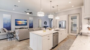 Una cucina moderna con mobili bianchi, un'isola centrale e illuminazione a sospensione.