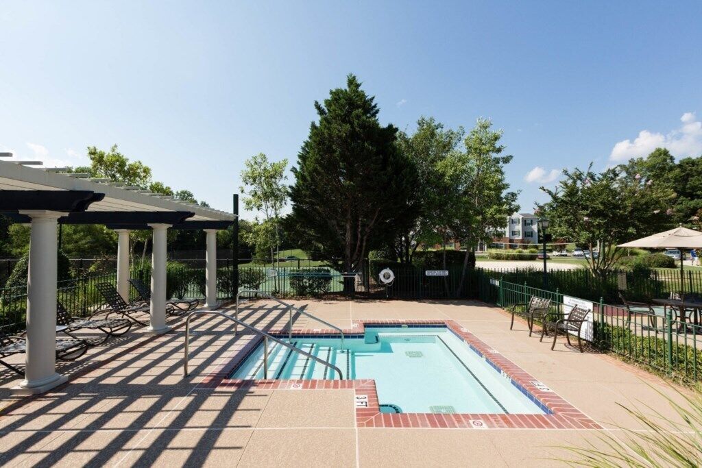 A rectangular swimming pool with a tiled deck, surrounded by a fence and shaded by a pergola.
