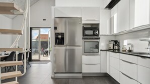 Et moderne køkken med indbygget køleskab, ovn og mikroovn. En spiseplads med et bord og stole kan ses gennem en åben dør.