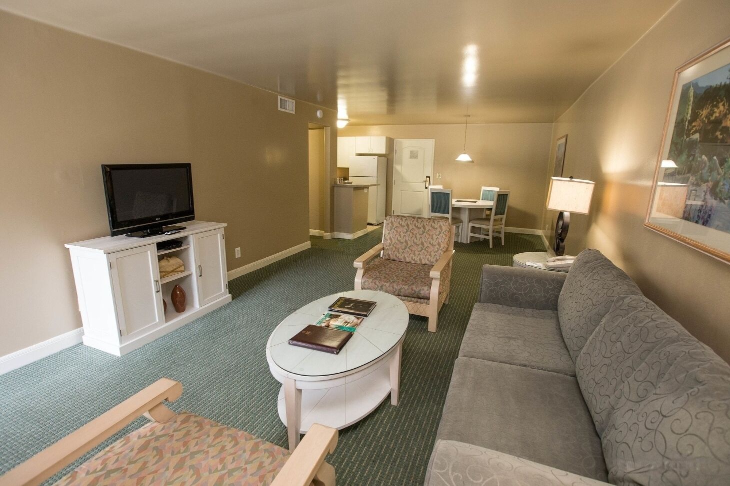Habitación de hotel con televisor, sofá, sillón, una mesita y un área de comedor con sillas.