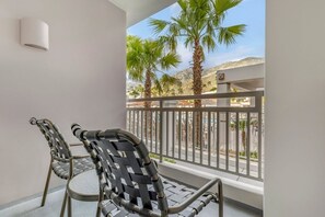 Un balcon avec deux chaises, un mur blanc et une vue sur des palmiers et une rue.