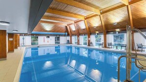 An indoor swimming pool with wooden beams, clear blue water, and a view of the outdoors. - Devon | Peaceful Country Escape | Pool + Sauna (Devon)