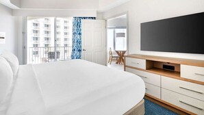 Una camera d'albergo con un letto grande, una scrivania con televisione a schermo piatto, una sedia e vista su un edificio dalla finestra.