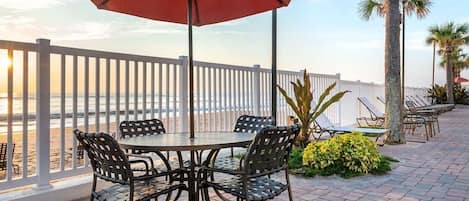 A patio with a round table and chairs, a red umbrella, and a view of the ocean.