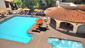 Ein großer Pool mit Liegestühlen und Sonnenschirmen, ein separater Whirlpool und eine überdachte Terrasse.