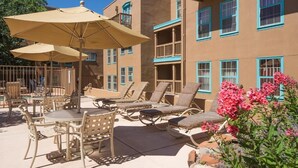 A patio with lounge chairs and umbrellas, a pool, and a building with balconies.