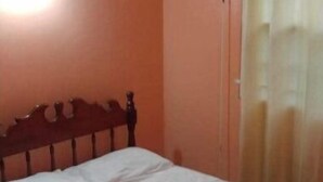 Ein Einzelbett mit Holz-Kopfstütze in einem Zimmer mit orangefarbenen Wänden und einem Fenster mit Vorhängen.