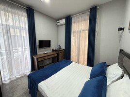 A hotel room with a bed, a desk, a television, and an air conditioning unit.