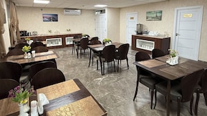 A hotel dining area with multiple tables and chairs, a coffee station, and a view of the cityscape.