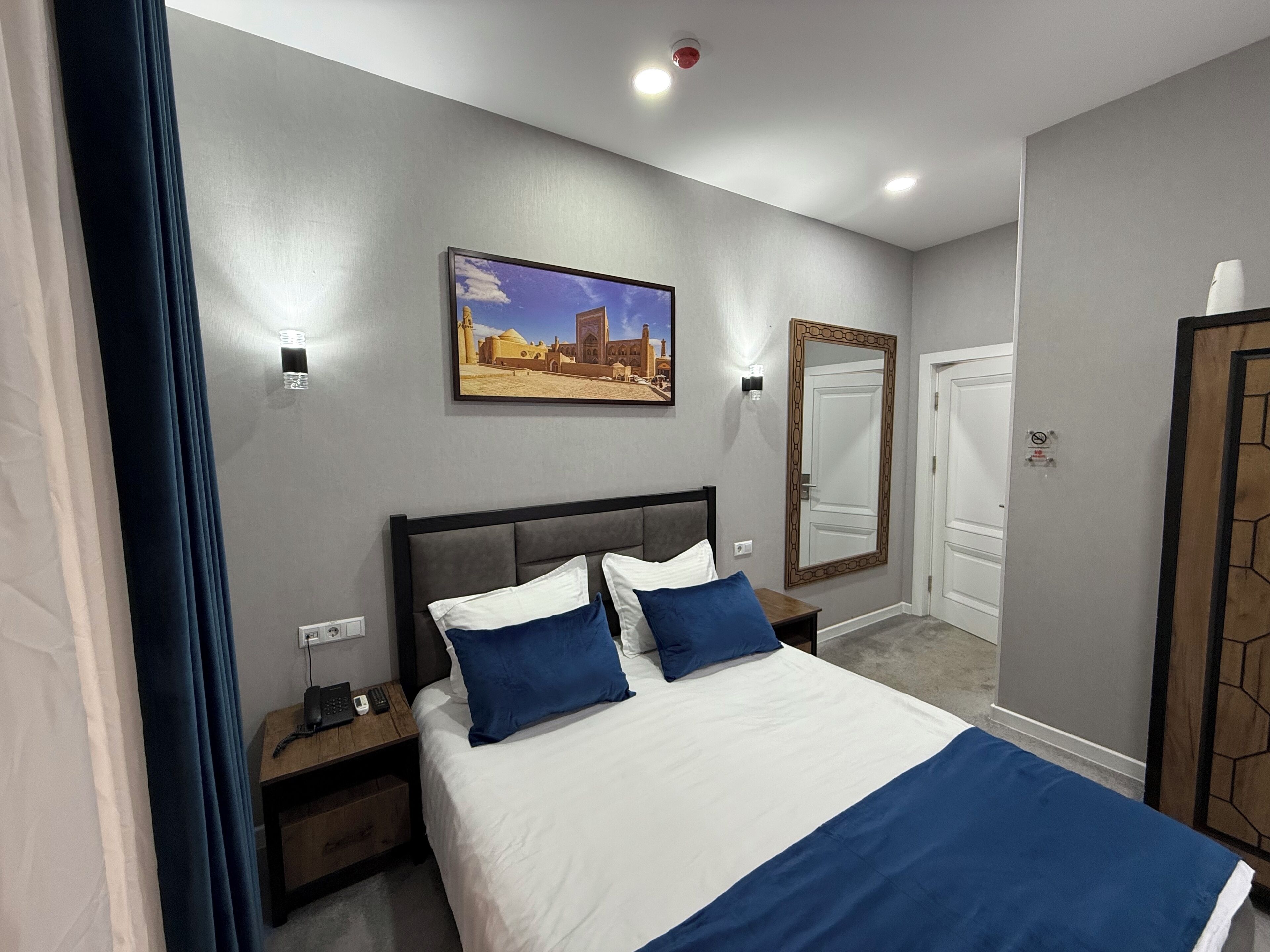 Quarto de hotel com cama, mesas de cabeceira, espelho e um quadro na parede.