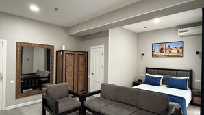 A hotel room with a bed, a sofa, a chair, a wardrobe, a mirror, and a picture on the wall.