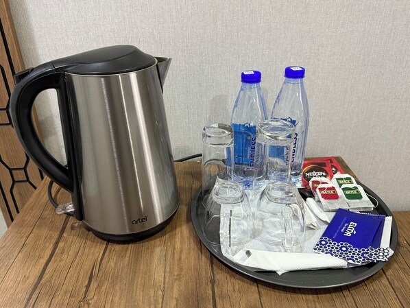 A stainless steel kettle, two water bottles, and a tray with napkins and sachets on a wooden table.