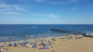 Une plage avec une jetée qui s’avance dans l’océan, de nombreux parasols et des gens qui profitent de la mer.