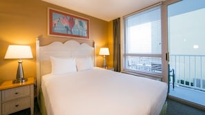 Habitación de hotel con una cama grande, dos mesitas de noche con lámparas, un cuadro en la pared y un balcón con barandilla.