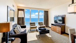 Ein Hotelzimmer mit einer Couch, Sesseln, einem Couchtisch, einem Fernseher und Blick auf den Ozean.