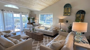 A spacious living room with a high wooden ceiling, large windows, and a cozy seating area with a sofa and armchairs.