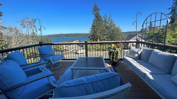A deck with outdoor seating, a view of a lake, and a forested area in the background.
