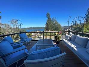 A deck with outdoor seating, a view of a lake, and a forested area in the background.