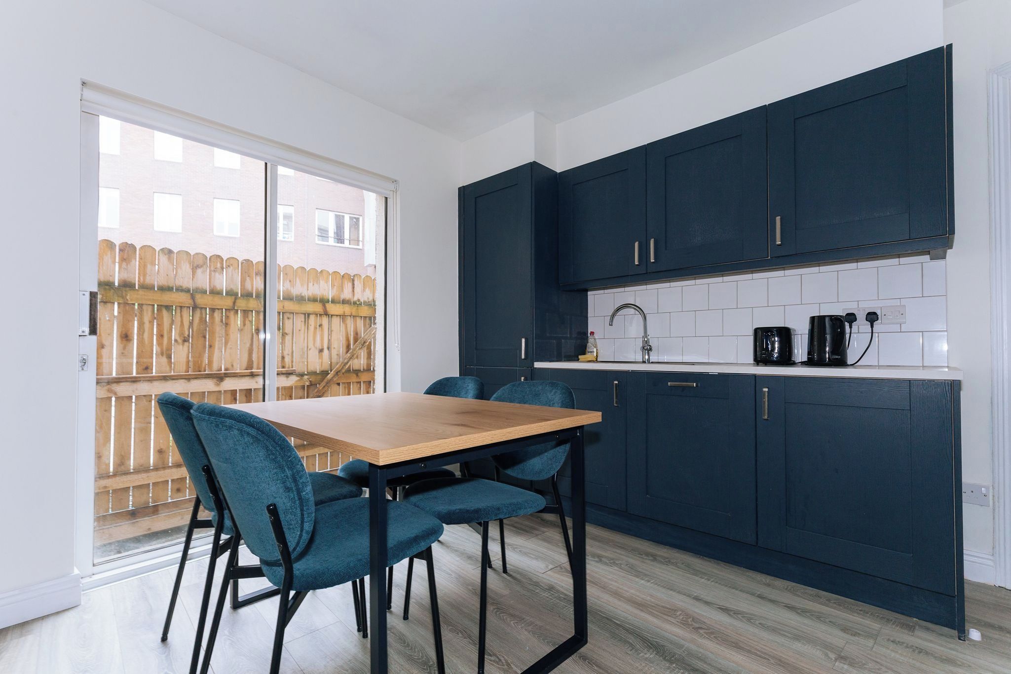 A modern kitchen with dark cabinets, a wooden table, and teal chairs.